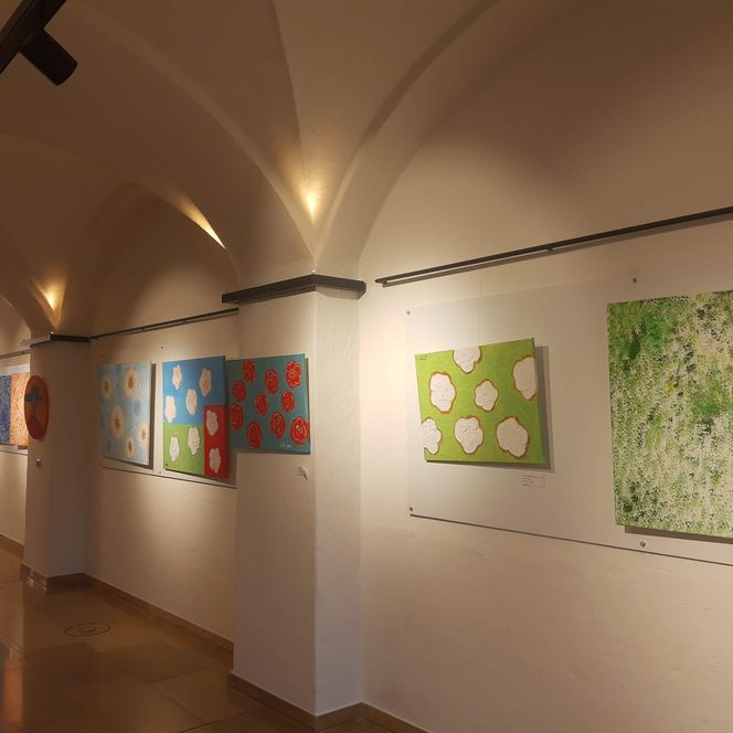 Mehrere Gemälde hängen an einer Wand und sind Teil einer Ausstellung im Foyer des Rathauses.
