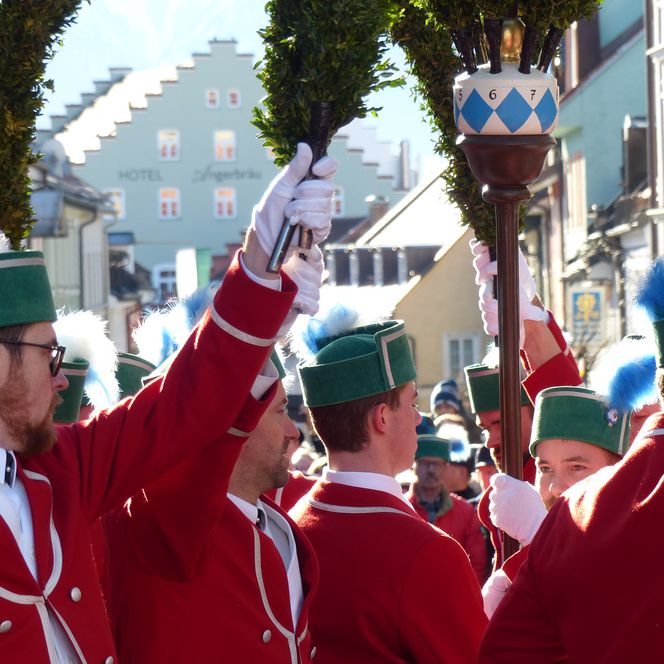 Schäffler in roter Tracht und grün geschmückten Bögen tanzen den Schäfflertanz.