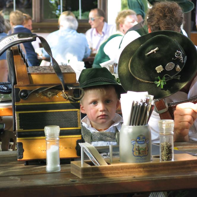 Kleiner Junge in Tracht am Tisch sitzend. 
