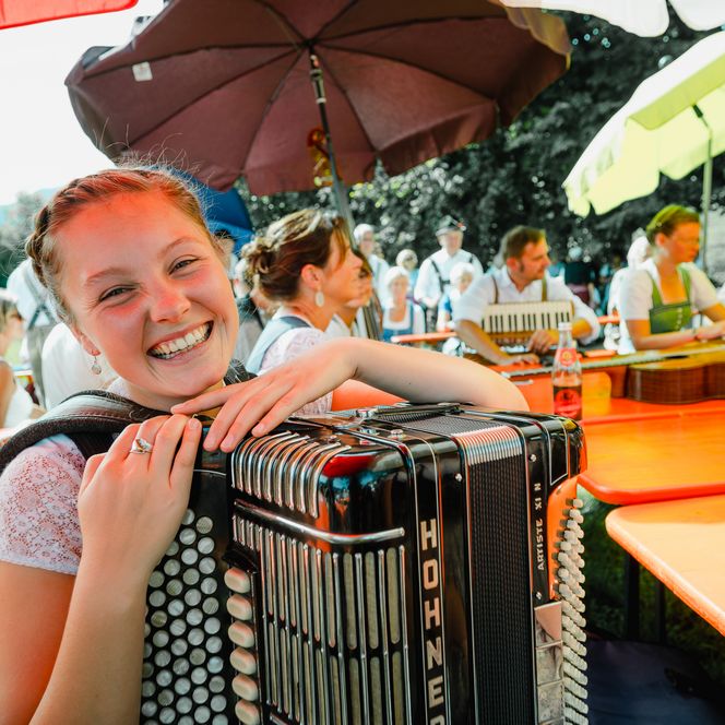 Eine Musikerin lächelt fröhlich in die Kamera. Im Hintergrund musizieren einige weiteren Musiker.