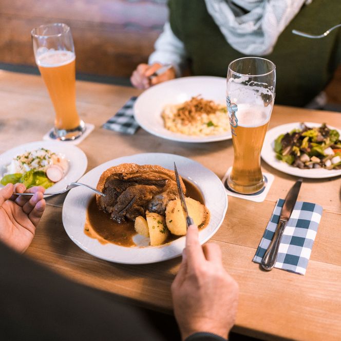 Schweinehaxe und Käsespätzle auf zwei Tellern mit zwei Gläsern Weißbier
