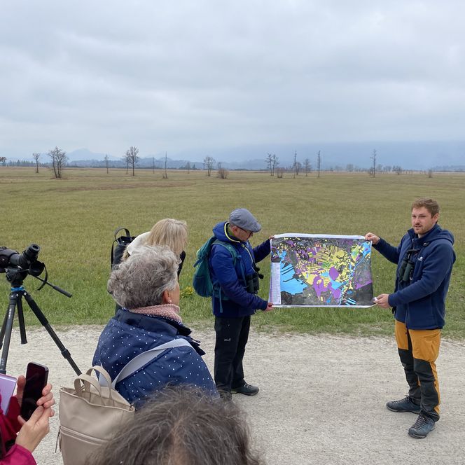 Personen hören zwei Gästeführern vor dem Murnauer Moos zu.