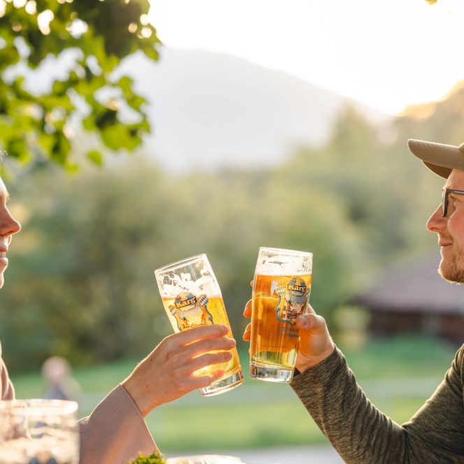 Zwei Personen stoßen im Biergarten mit Biergläsern an.