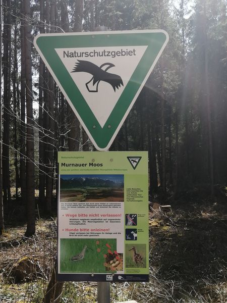 Schild, das ein Naturschutzgebiet ausweist mit Informationstafel.