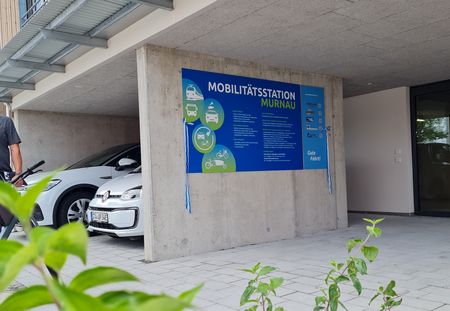 Mobilitätsstation am Bahnhof mit Informationstafel und E-Autos zum Ausleihen.