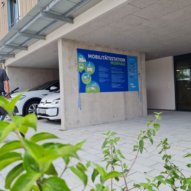 Außenansicht der Mobilitätsstation mit Informationstafel und E-Autos zum Ausleihen.
