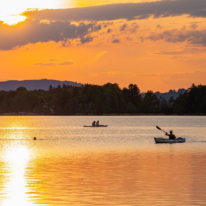 Ein Kajakfahrer paddelt auf dem Staffelsee bei Sonnenuntergang.
