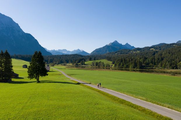 Grüne Wiese mit See im Hintergrund und einem Radweg, auf dem zwei Radfahrer fahren.
