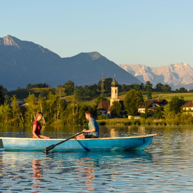 Ein Paar sitzt in einem Ruderboot, im Hintergrund sind Froschhausen und die Bergkette zu sehen.