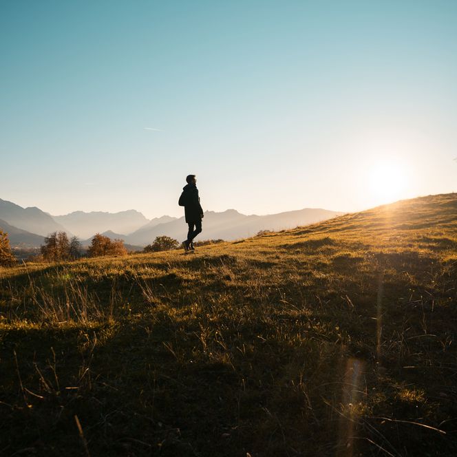Eine Person wandert bei Sonnenuntergang über eine Wiese.