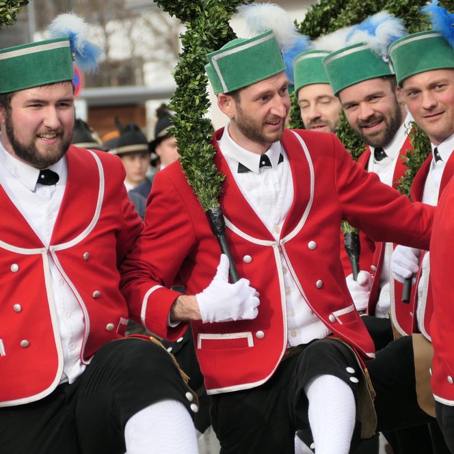 Schäffler tanzen in ihrer traditionellen roten Tracht und halten grün geschmückte Bögen während des Schäfflertanzes.