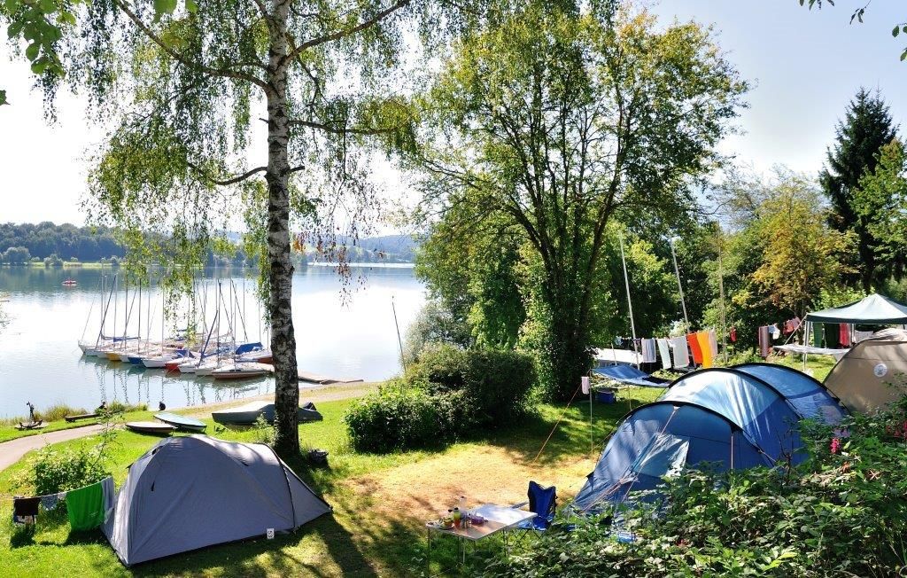 Drei Zelte auf einem Zeltplatz am Ufer eines Sees.