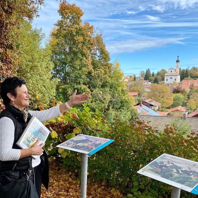 Eine Gästeführerin zeigt auf einen Aussichtspunkt mit Blick auf das Schloßmuseum Murnau und die St. Nikolauskirche, wie ihn Künstler des Blauen Reiters gemalt haben.