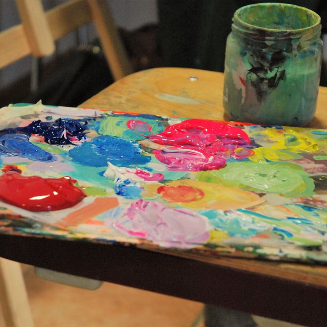 Bunte Farbpalette auf dem Tisch liegend im Hintergrund eine Staffelei