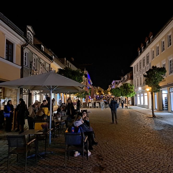 Fußgängerzone bei Nacht, im linken Bildrand teilnehmende Gastronomie