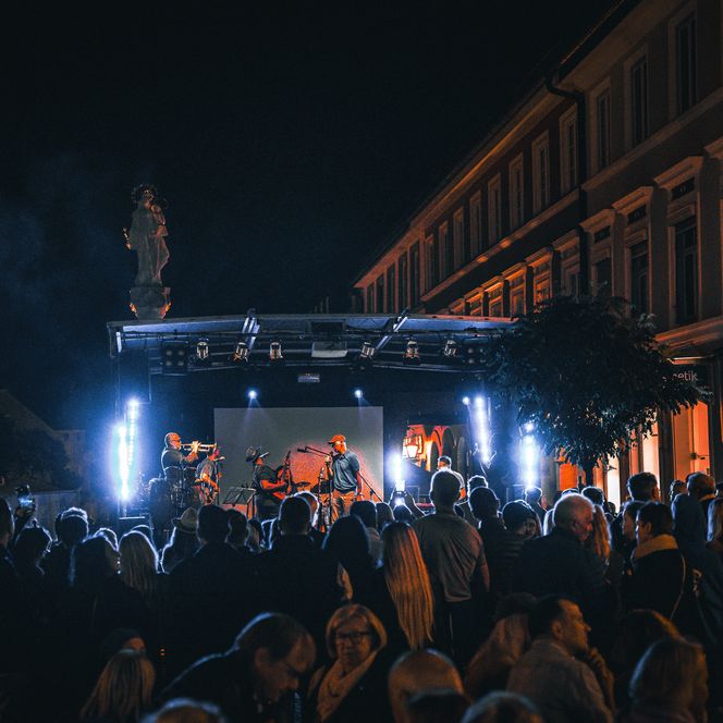 Im Hintergrund eine große Musikbühne bei Dunkelheit mit Blick Richtung Süden, im Vordergrund viele Menschen
