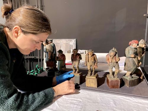 Eine Frau zeigt alte Figuren aus Holz.